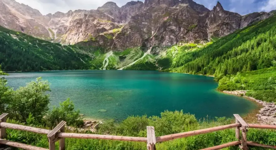 Turkusowe jezioro otoczone zielonymi zboczami gór, przypominające beskidzkie Morskie Oko.