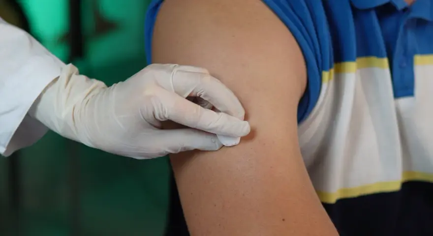 Ręka w rękawiczce dezynfekuje ramię przed podaniem zastrzyku. To przygotowanie do iniekcji śródskórnej.