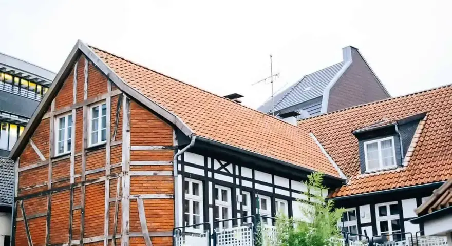 Tradycyjna **konstrukcja muru pruskiego** z ceglanymi wypełnieniami i drewnianymi belkami, obok nowoczesnych budynków.