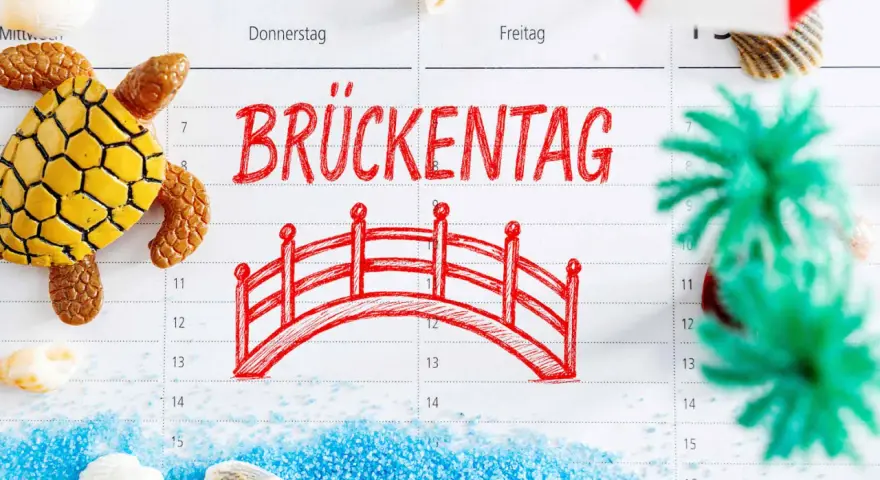 Kalenderblatt mit "Brückentag" und einer roten Brücke, Schildkröte, Muscheln und Dekoration.