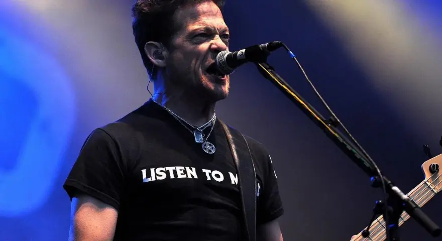 Jason Newsted z zespołu, w czarnej koszulce z napisem "LISTEN TO N", śpiewa do mikrofonu, grając na basie.