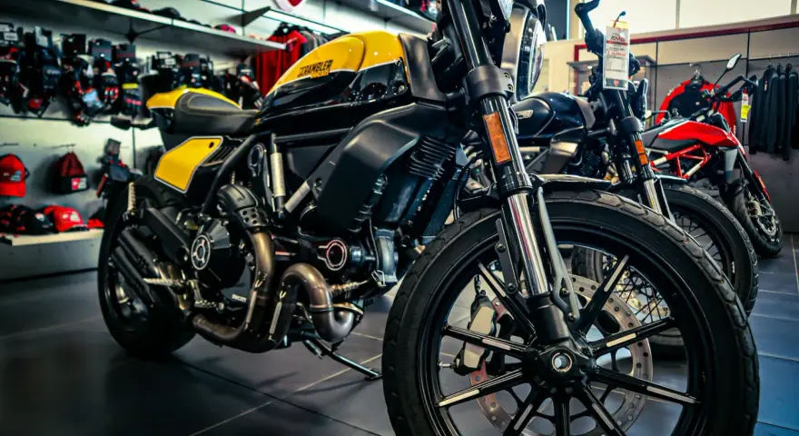 Ducati Scrambler gialla e nera, pronta per i raduni moto. Dietro, altre moto e abbigliamento tecnico.