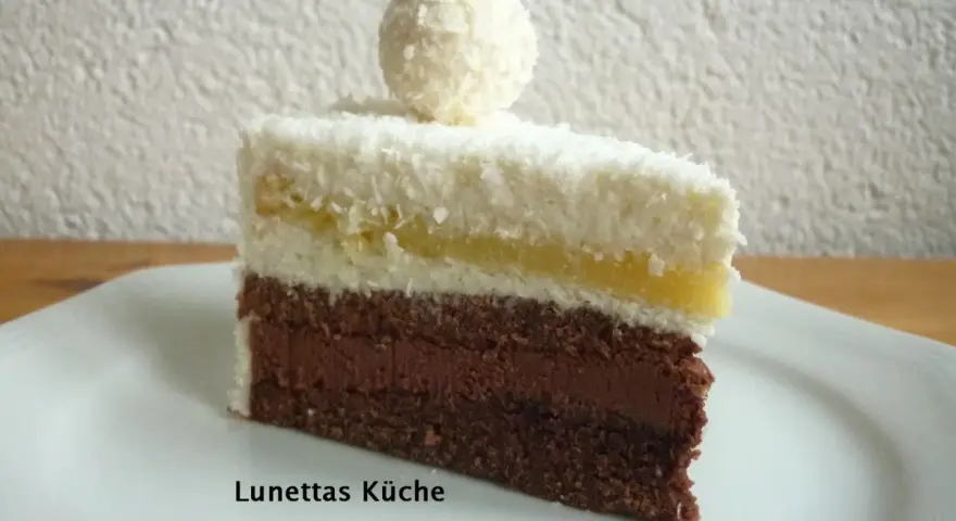 Ein Stück Schoko Kokos Torte mit Kokosraspeln und einer Praline obendrauf.