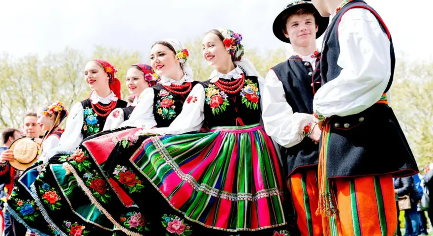 Młodzi ludzie w barwnych strojach ludowych, gotowi do wykonania polskich tańców narodowych.