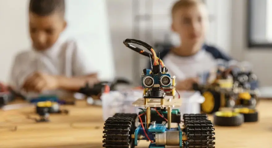 Dzieci budują roboty, ucząc się programowania i inżynierii. W centrum mały robot z czujnikami, w tle chłopcy pracujący nad projektami.