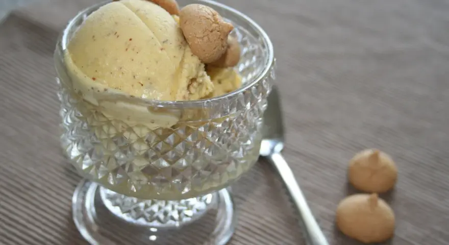 Ein Glas mit cremigem Marzipan Eis, garniert mit kleinen Keksen. Daneben liegen zwei weitere Kekse und ein Löffel.