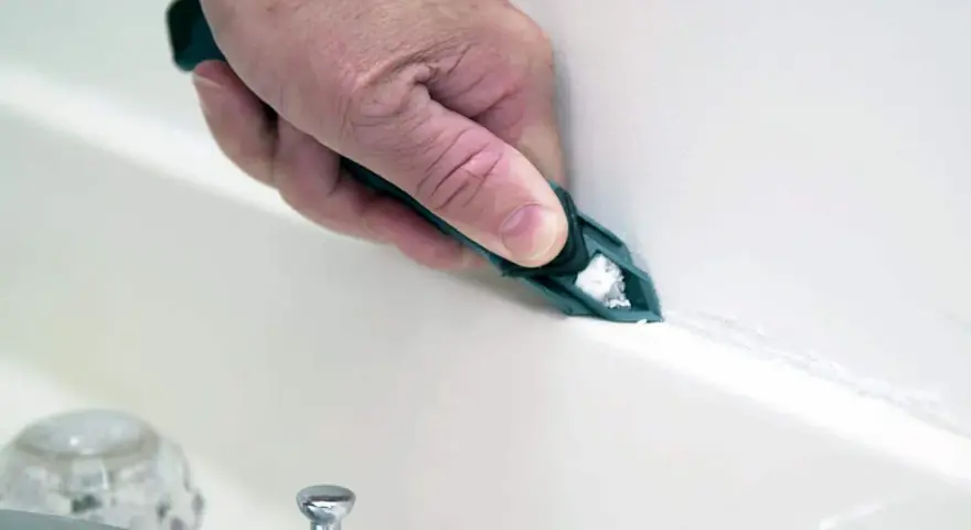 A hand uses a tool to smooth fresh caulk along a bathtub seam, demonstrating how to caulk for a clean finish.