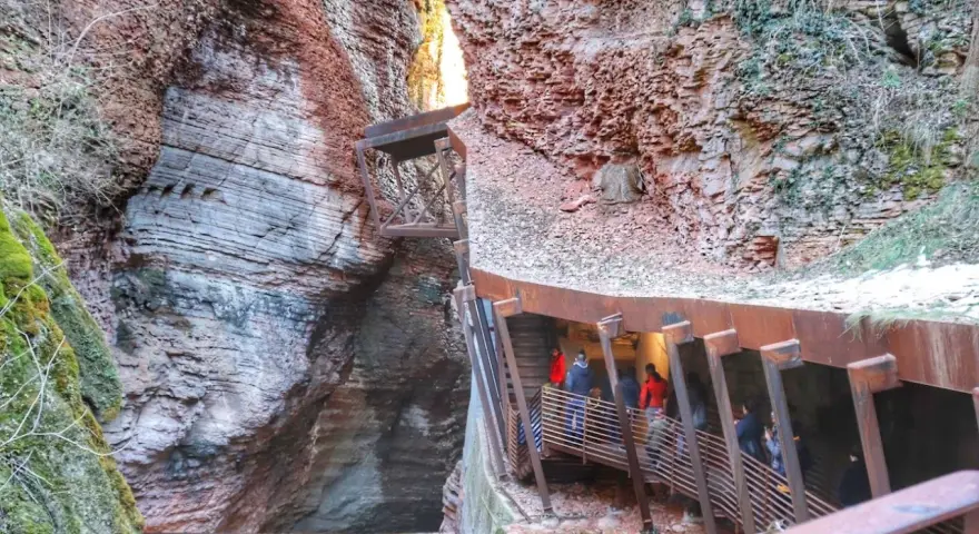Un orrido ponte alto attraversa una gola rocciosa, con persone che salgono una scalinata metallica.