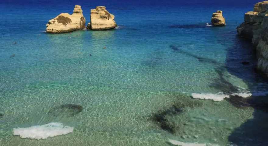 Un mare bello in Italia, con scogli dorati che emergono da acque cristalline e turchesi. Alcune persone nuotano in questo paradiso.