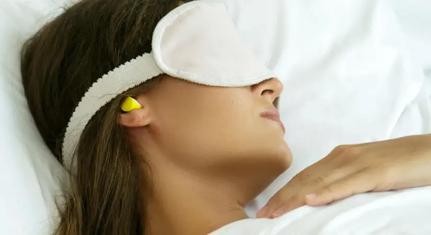 Femme dormant avec un masque et des boules quies pour éviter le bruit, utile en cas d'otite ou pour un sommeil paisible.