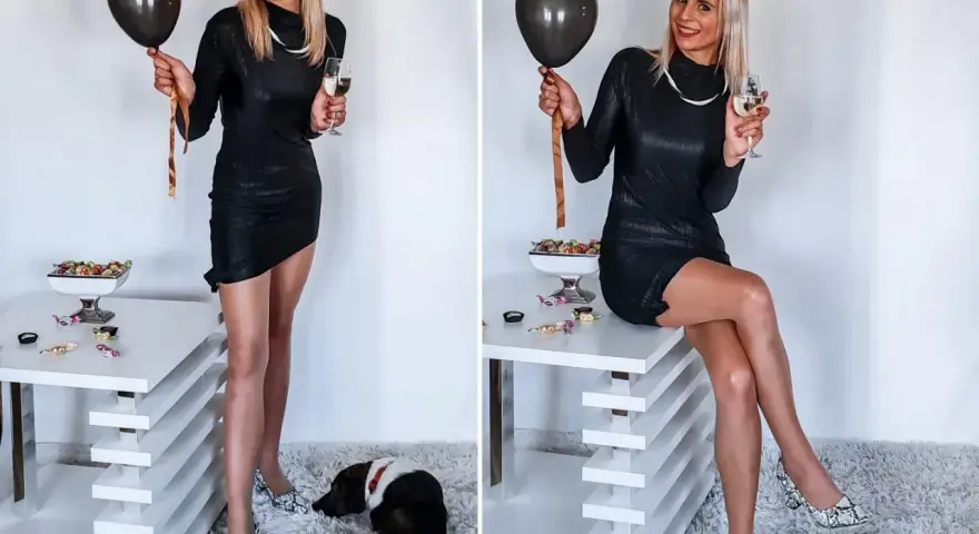 Elegancka czarna sukienka, idealna na 18. urodziny. W dłoni czarny balon i kieliszek szampana. Na podłodze leży piesek.