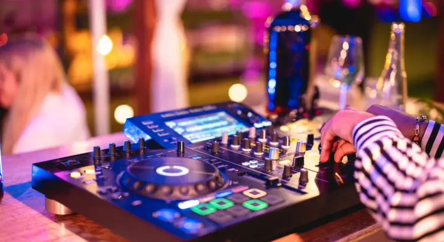 Main d'un dj house connu manipulant la console, lumières vives et ambiance festive.