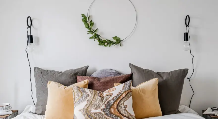 Mysigt sovrum inspiration med en rund väggdekoration av gröna blad, flera kuddar i olika färger och texturer, samt svarta vägglampor.