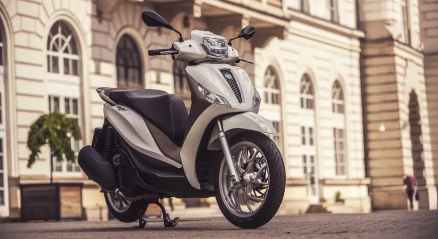 Biały skuter Piaggio Medley zaparkowany na bruku przed zabytkową kamienicą.