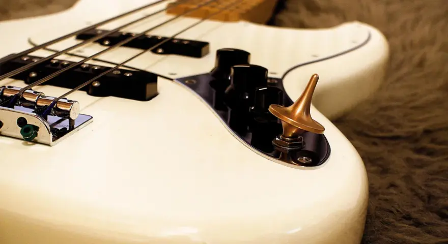 Ein weißes Bassmusikinstrument mit vier Saiten und einem bronzenen Kreisel auf dem Bedienfeld.