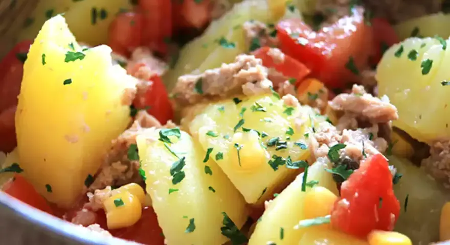 Salade de pommes de terre, thon, tomates et maïs, parsemée de persil frais. Un plat simple et savoureux.