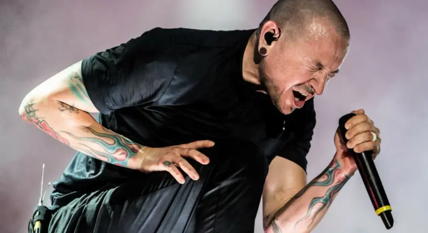 Chester Bennington z Linkin Park, z tatuażami na ramionach, śpiewa do mikrofonu z pasją.