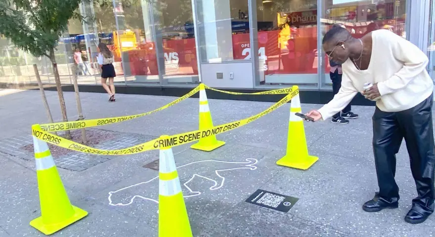 Ein Mann scannt mit seinem Handy einen QR-Code neben einer Kreideumriss-Leiche. Ein cleveres Guerilla-Marketing-Event.