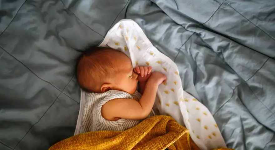 Noworodek śpi otulony kocykami. Skóra dziecka ma lekko żółtawy odcień, co może sugerować żółtaczkę u noworodka.