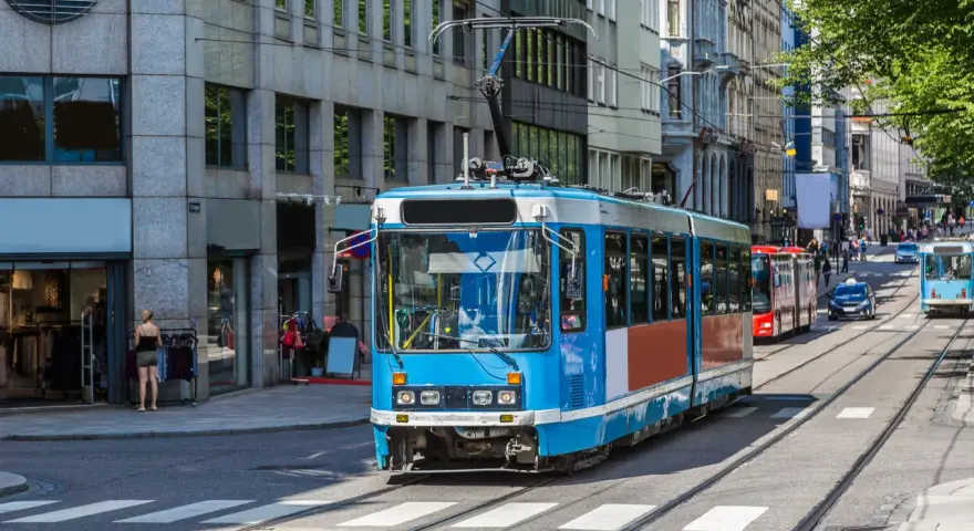 Błękitny tramwaj na tle budynków w Oslo. To część sprawnie działającej oslo komunikacji miejskiej, która przewozi mieszkańców i turystów.