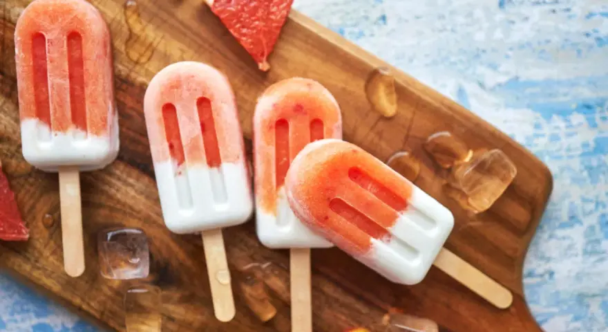 Erfrischendes Erdbeereis auf Holzbrett, mit Eiswürfeln und Grapefruitstücken. Perfekt für heiße Tage, wenn man Kalorien im Blick behält.