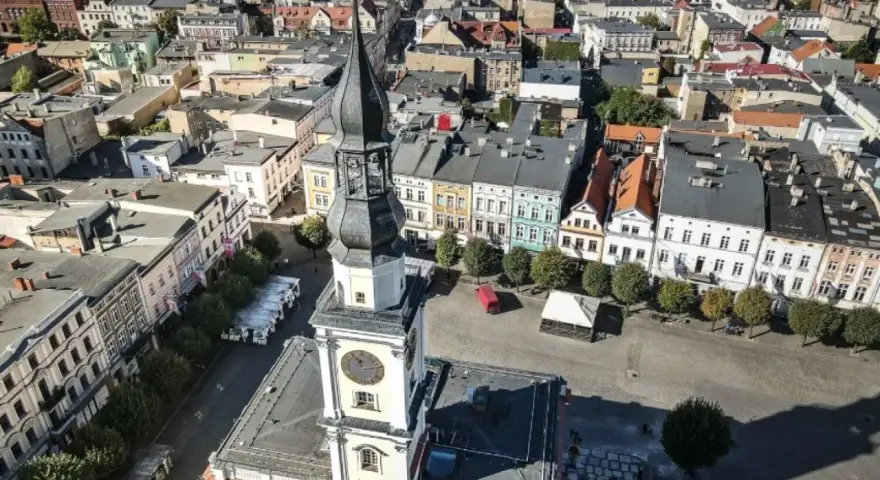 Widok z lotu ptaka na rynek w Lesznie. Wieża ratusza góruje nad kolorowymi kamienicami, ukazując urokliwe leszno atrakcje.