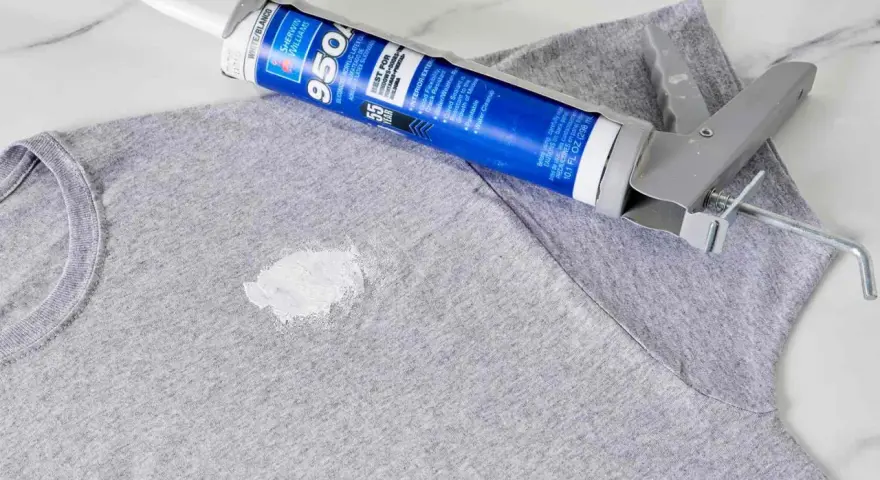 Zaschnięty silikon na szarym T-shircie i pistolet do jego aplikacji. Dowiedz się, jak usunąć zaschnięty silikon z ubrania.