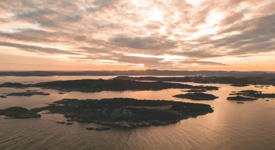 Zachód słońca nad archipelagiem, przypominającym szwedzkie fiordy. Woda odbija złote światło, a chmury malują niebo.