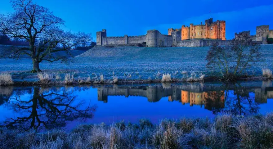 Un château majestueux se reflète dans l'eau calme, sous un ciel d'un bleu profond. Une scène paisible de **heure bleue photo**.