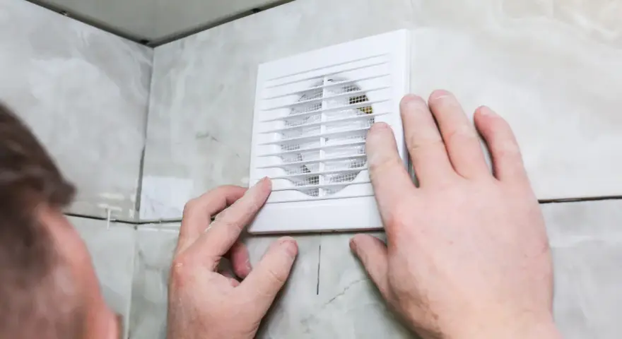 Installation d'un nouveau ventilateur pour la **salle de bain ventilation**. Mains ajustant l'appareil blanc sur un mur carrelé.