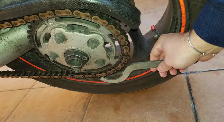 Mano con chiave speciale per regolare la catena della moto, mostrando come tirare la catena.