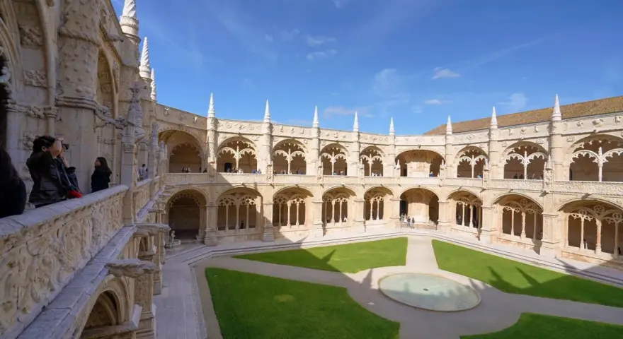 The Jerónimos Monastery, a stunning monastery in Portugal, features a grand courtyard with intricate stonework and a lush green lawn.
