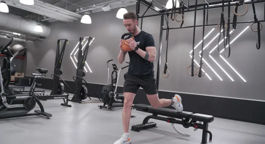 Man tränar utfall med kettlebell i ett modernt gym. Han fokuserar på att bygga en stor rumpa.