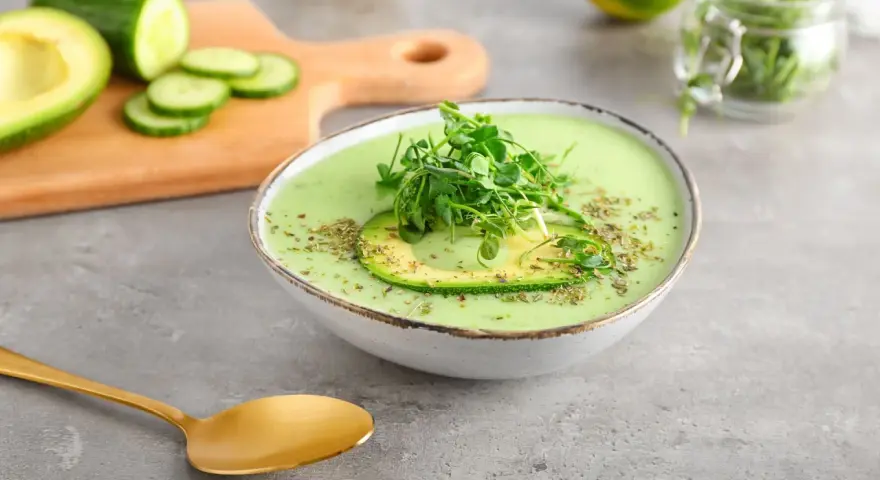 Gazpacho de aguacate cremoso con rodaja de aguacate y brotes verdes, servido en un cuenco blanco.