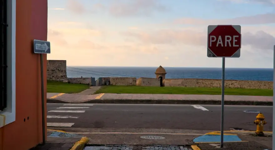 A "PARE" sign stands by the ocean in Puerto Rico. Should I rent a car to explore this beautiful island?