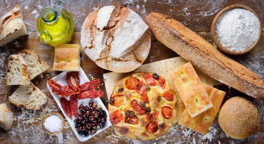 Apulia jedzenie: świeże pieczywo, focaccia z pomidorami, oliwki, suszone pomidory i oliwa z oliwek na drewnianym stole.