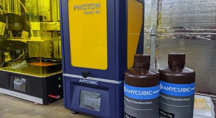 Dwa drukarki 3D Anycubic, w tym Anycubic Photon Mono SE, oraz butelki z żywicą do druku.