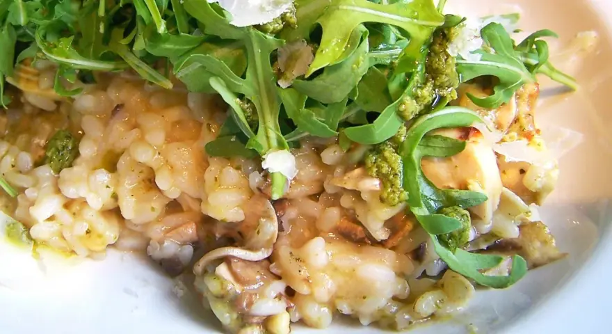 Kremowe risotto z kurczakiem i pieczarkami, udekorowane rukolą i parmezanem.