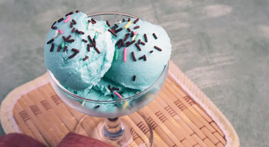 Ein Glas mit drei Kugeln blaues Eis, bestreut mit Schokostreuseln und bunten Zuckerstreuseln.