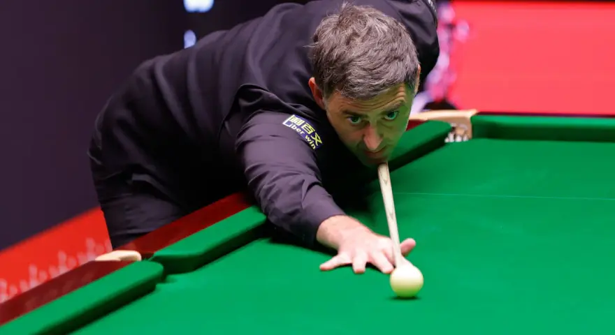 Ronnie O'Sullivan, jeden z najlepsi snookerzyści wszechczasów, skupiony przy zielonym suknie, celuje w bilę.