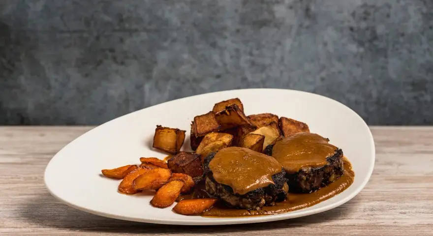 Delicioso rabo de toro bañado en salsa, acompañado de patatas rústicas y zanahorias glaseadas.