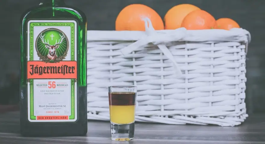 Butelka Jägermeistera i shot z dwoma warstwami, obok koszyk z pomarańczami. Idealne na wieczór, jak pić jagermeister.