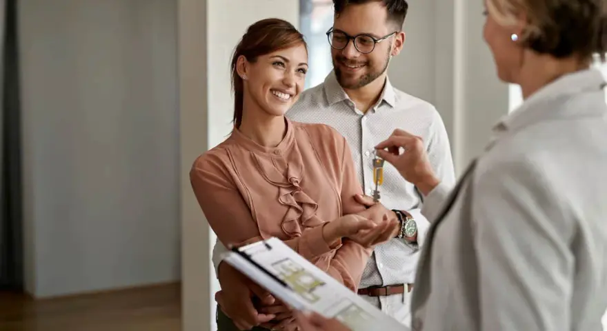 Pareja feliz recibe las llaves de su nuevo hogar, con un agente inmobiliario mostrando las escrituras de una casa.