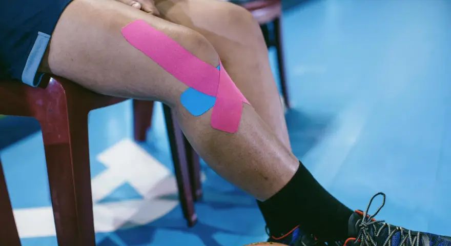 Sportowiec z plastrami na kolanie, przygotowujący się do ćwiczeń na chondromalację rzepki.