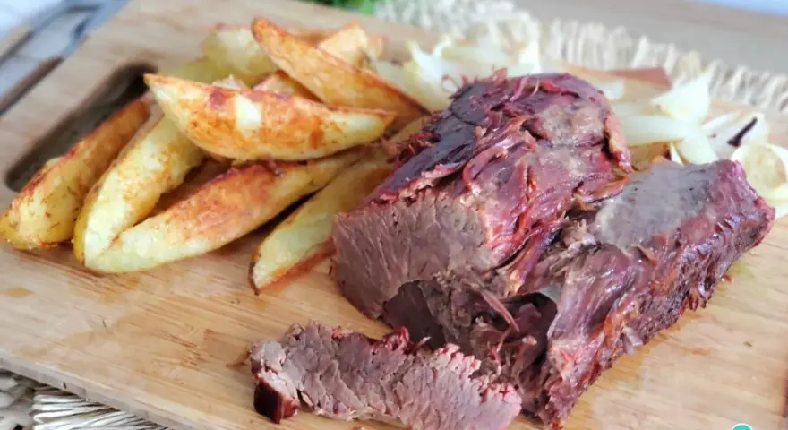 Rosbif jugoso y tierno servido con papas gajo y cebolla en una tabla de madera.