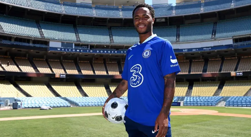 Raheem Sterling w niebieskiej koszulce Chelsea z piłką, na tle stadionu. Jego statystyki w klubie są obiecujące.