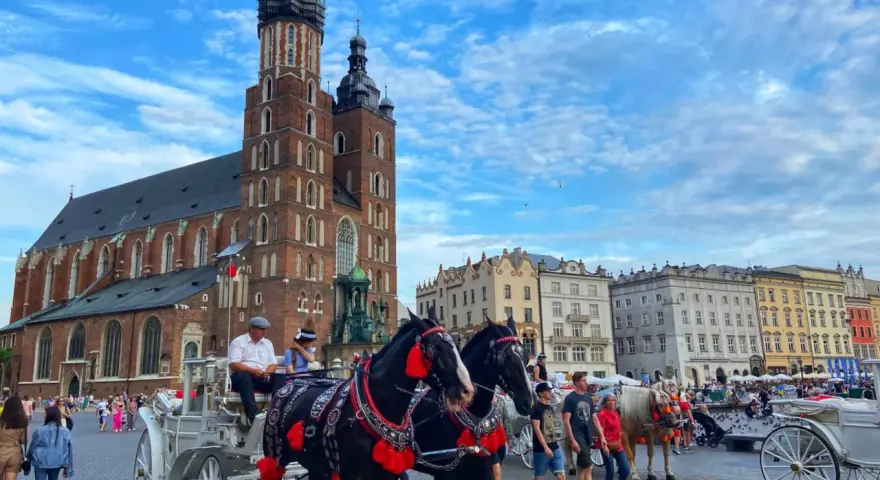 Horse-drawn carriages await tourists in Krakow's Old Town, a picturesque scene from a Poland trip, with St. Mary's Basilica towering in the background.