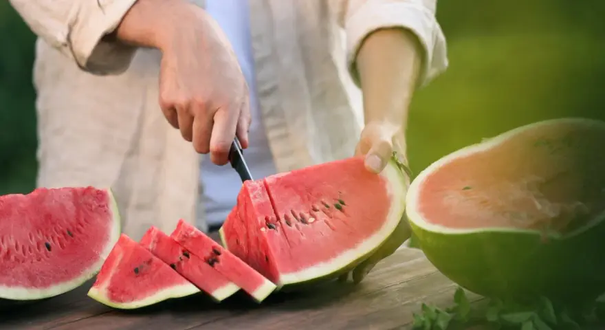 Mężczyzna kroi soczystego arbuza, pokazując, jak wybrać dobrego arbuza. Na stole leżą już pokrojone kawałki.