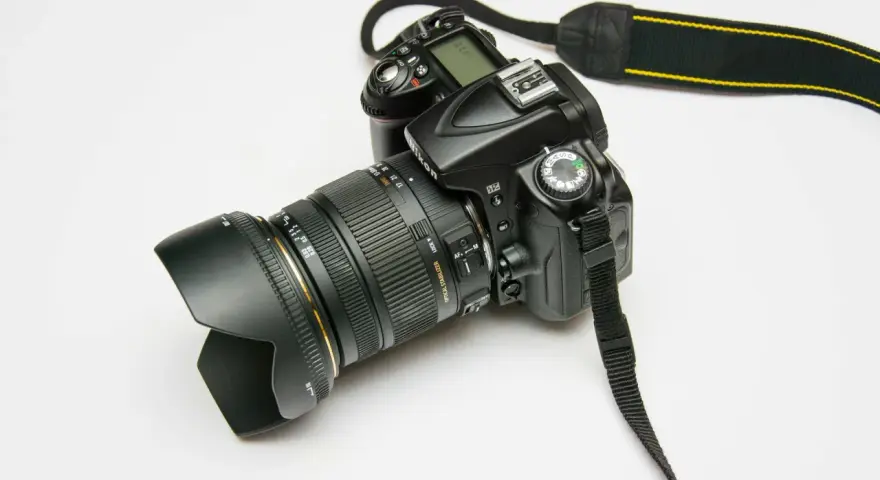 Czarna lustrzanka cyfrowa Nikon z obiektywem i paskiem na białym tle.