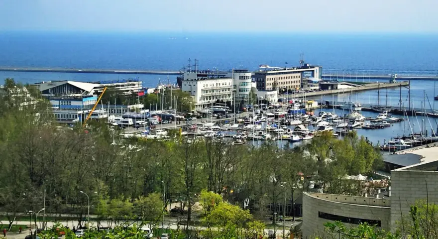 Widok na port jachtowy w Gdyni z licznymi łodziami i budynkami w tle.